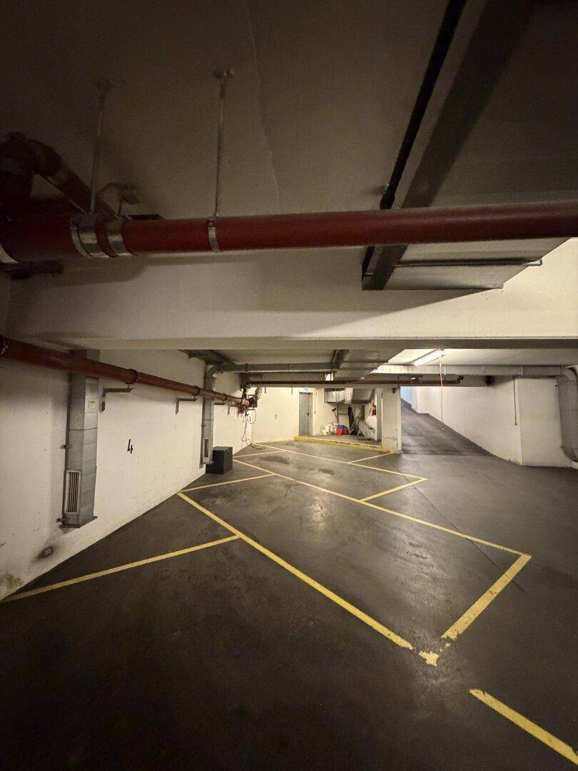 Weitläufige Tiefgarage mit gelb markierten Parkplätzen und einer Rampe, die zum Ausgang führt.