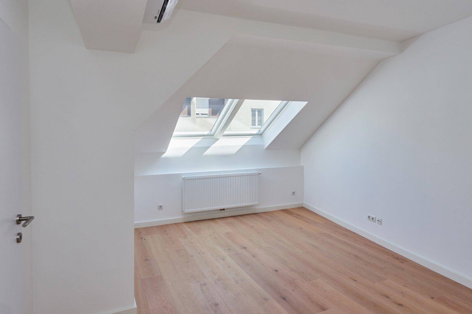 Helles Schlafzimmer im Dachgeschoss mit Holzboden, Klimaanlage und einem großen Dachfenster.