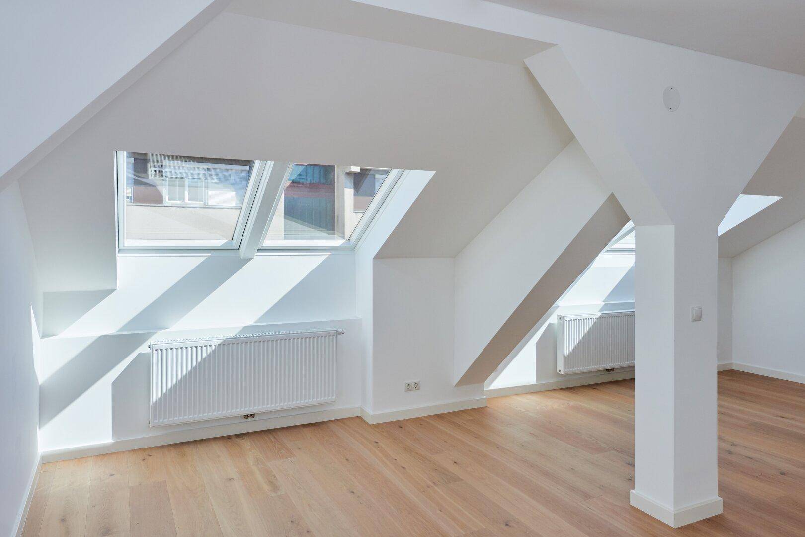 Sonnendurchfluteter Dachgeschossraum mit Holzboden, Heizkörpern und großen Dachfenstern.