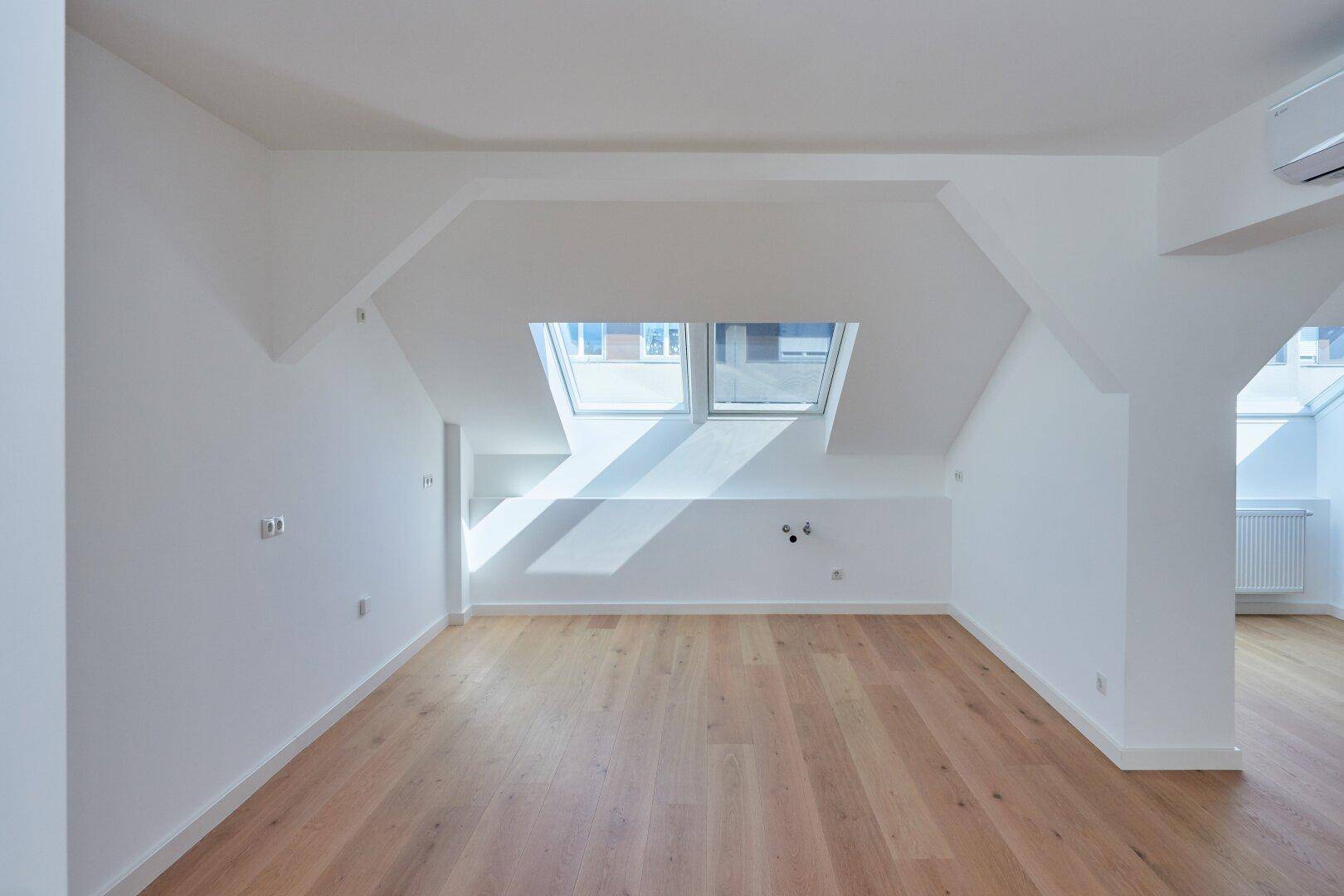 Geräumiger Dachgeschossraum mit Holzboden, Klimaanlage und zwei großen Dachfenstern.