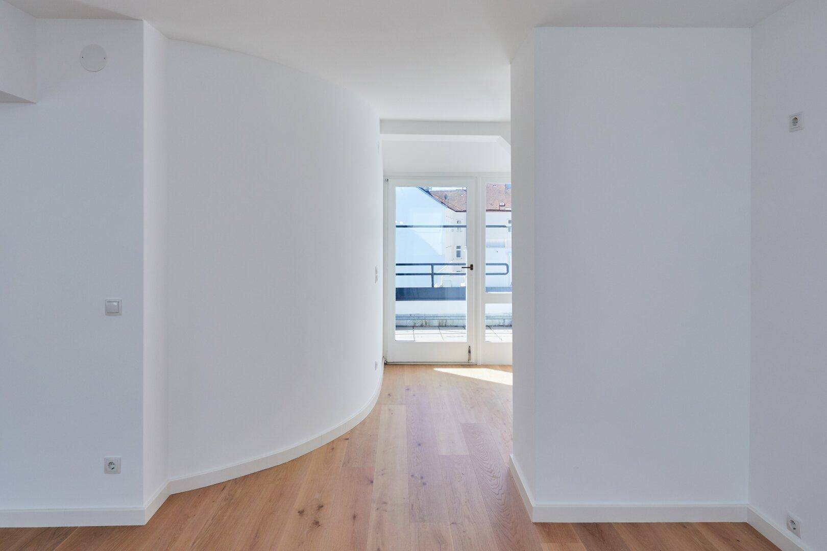 Heller Flur mit Holzboden und einer eleganten Rundwand, die zum Außenbereich führt.
