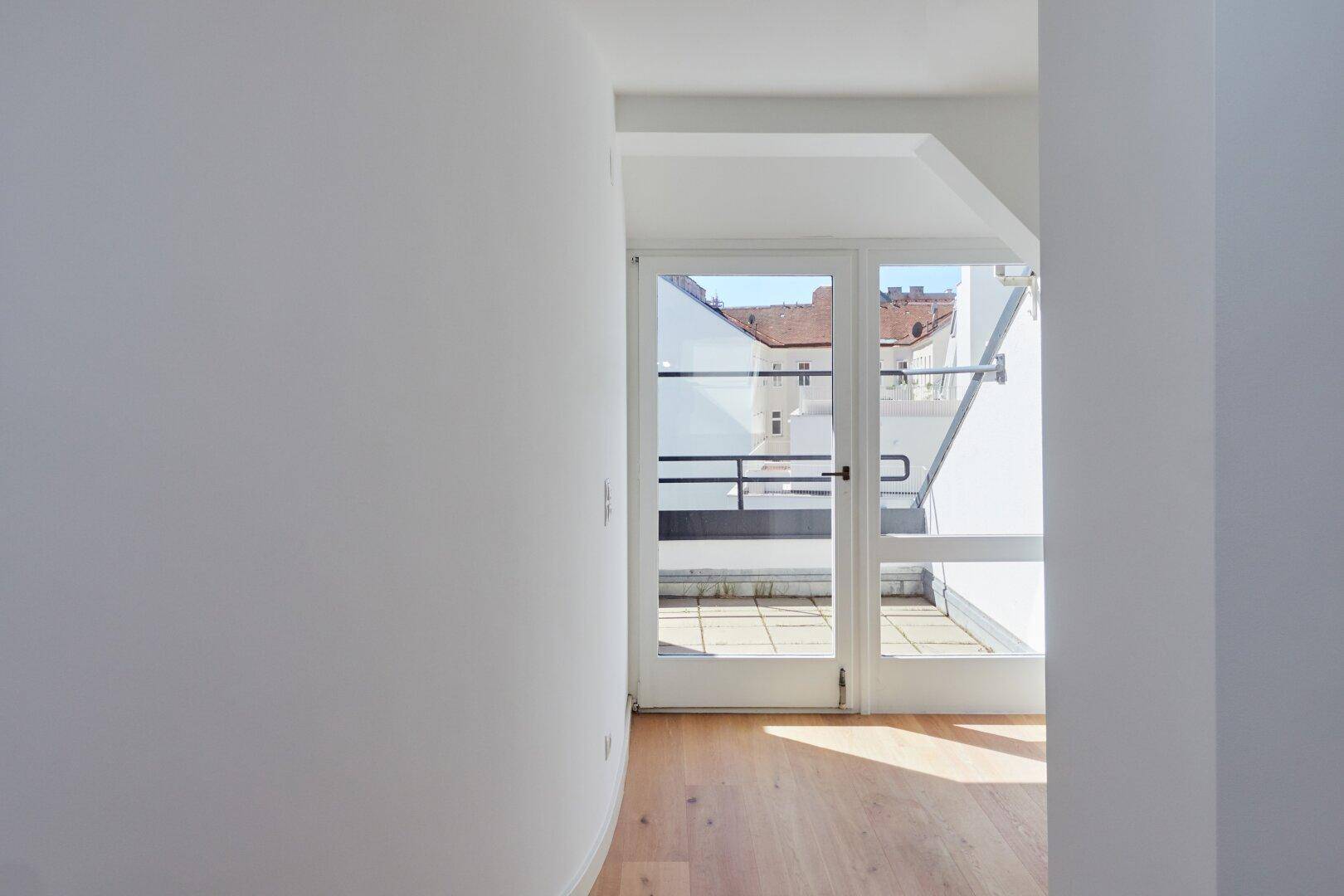 Flur mit Holzboden und Glastür, die Zugang zu einer sonnigen Dachterrasse bietet.