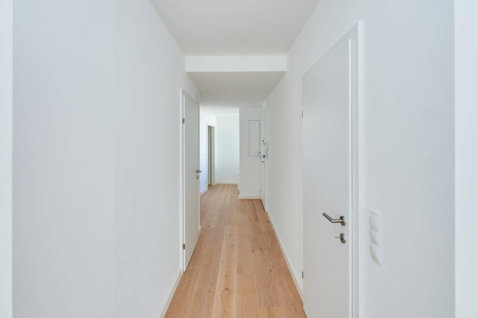 Langer, heller Flur mit Holzboden und weißen Türen, der zu verschiedenen Räumen führt.