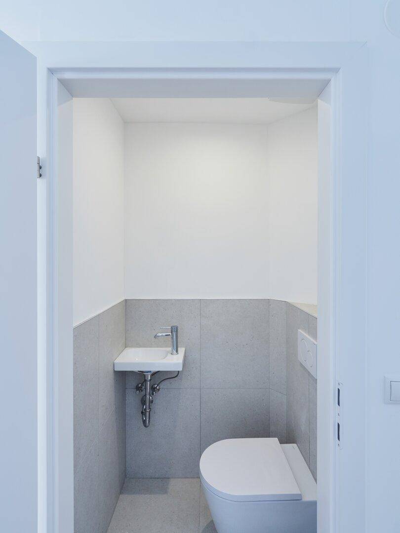Kleines Gäste-WC mit wandmontierter Toilette, Handwaschbecken und modernen Fliesen.