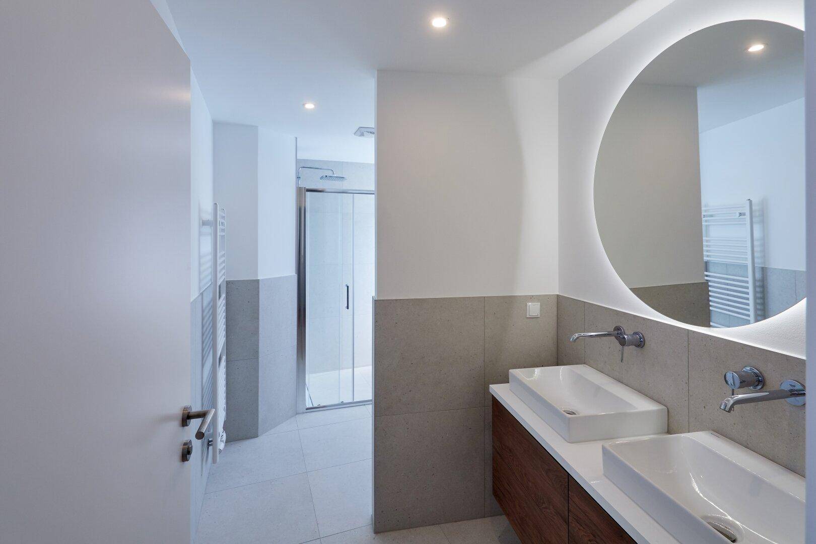 Modernes Badezimmer mit Doppelwaschbecken, beleuchtetem Spiegel und separater Dusche.