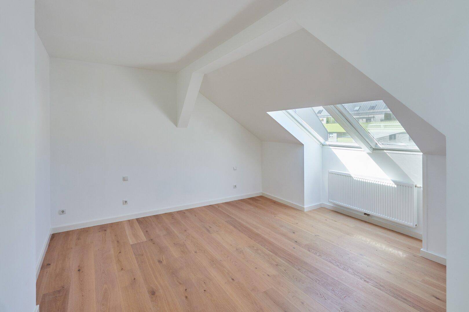 Ruhiges Schlafzimmer im Dachgeschoss mit Holzboden, schrägen Wänden und Dachfenster.