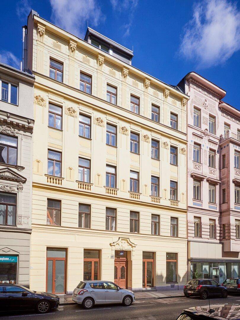 Historisches Gebäude mit reich verzierter Fassade und klassischen Fenstern an einer Stadtstraße.
