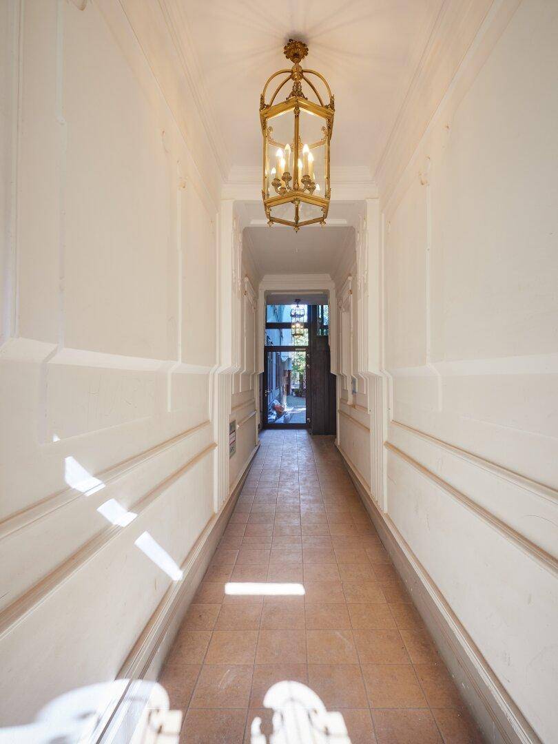 Eleganter Eingangsbereich mit Fliesenboden und klassischer Deckenleuchte, führt zum Hinterhof.