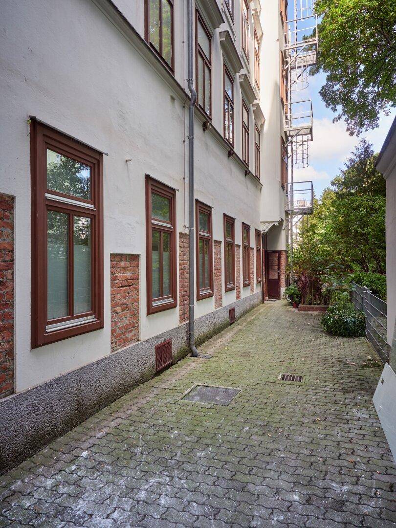 Seitenweg zwischen Gebäuden mit Pflastersteinen und Blick auf die Rückseite des Hauses.