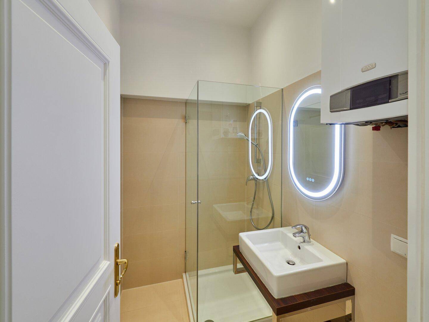 Helles Badezimmer mit Glasdusche, modernem Waschtisch und beleuchtetem Spiegel.