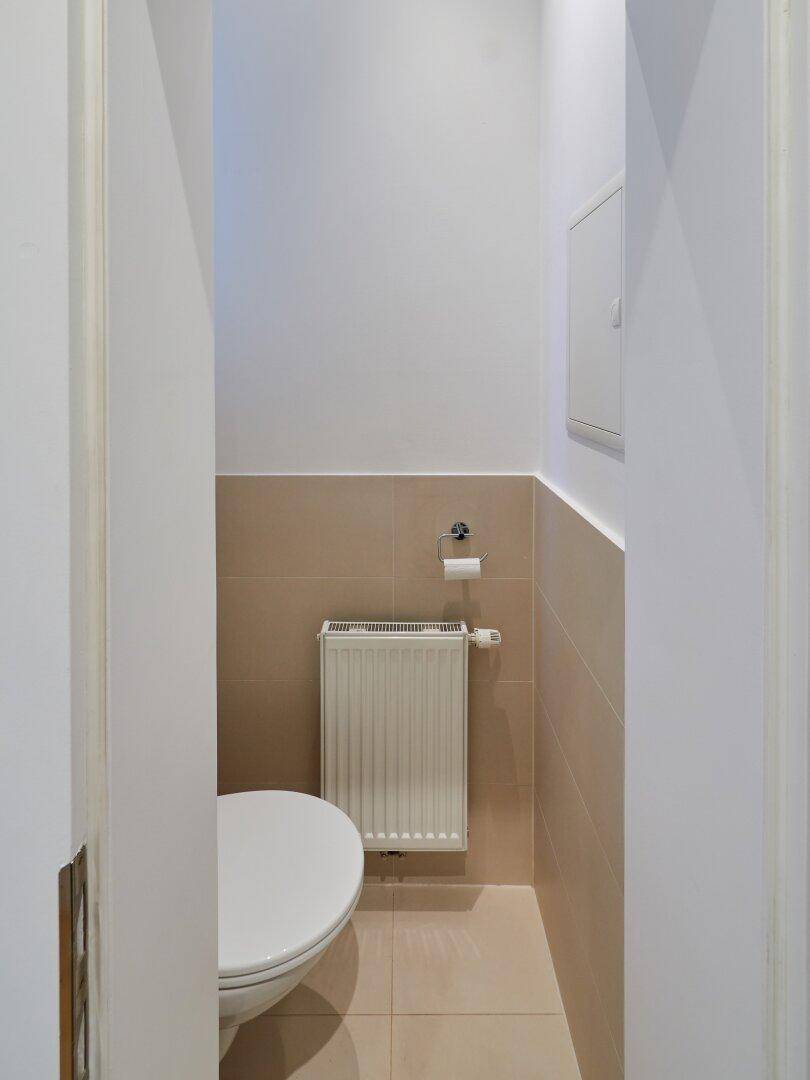 Kleines Gäste-WC mit Wand-WC und beigefarbenen Fliesen, inklusive Heizkörper.