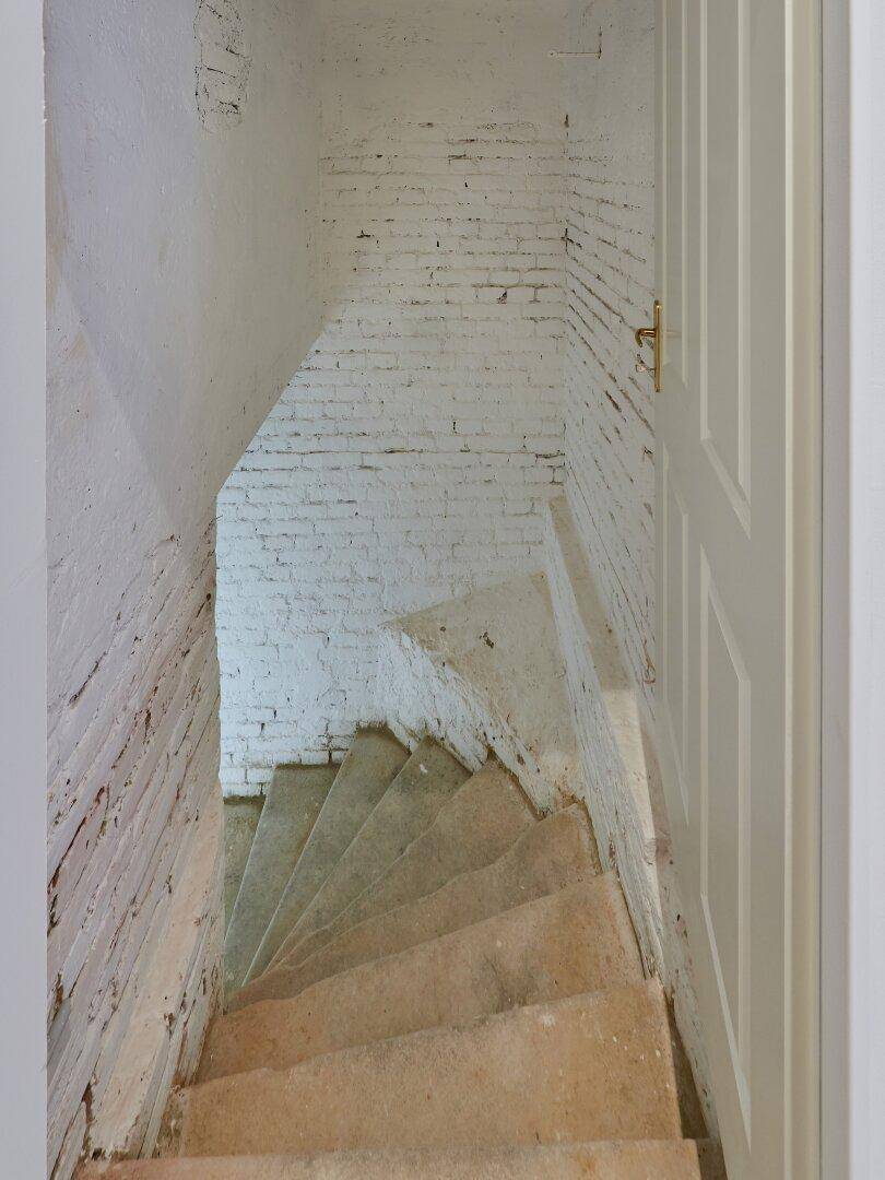 Steintreppe führt hinunter in den Kellerbereich mit unverputzten Ziegelwänden.