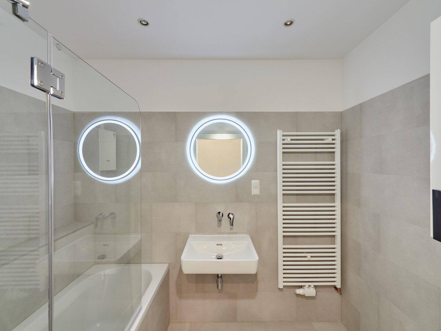 Modernes Badezimmer mit Badewanne, beleuchteten Spiegeln und beheiztem Handtuchhalter.