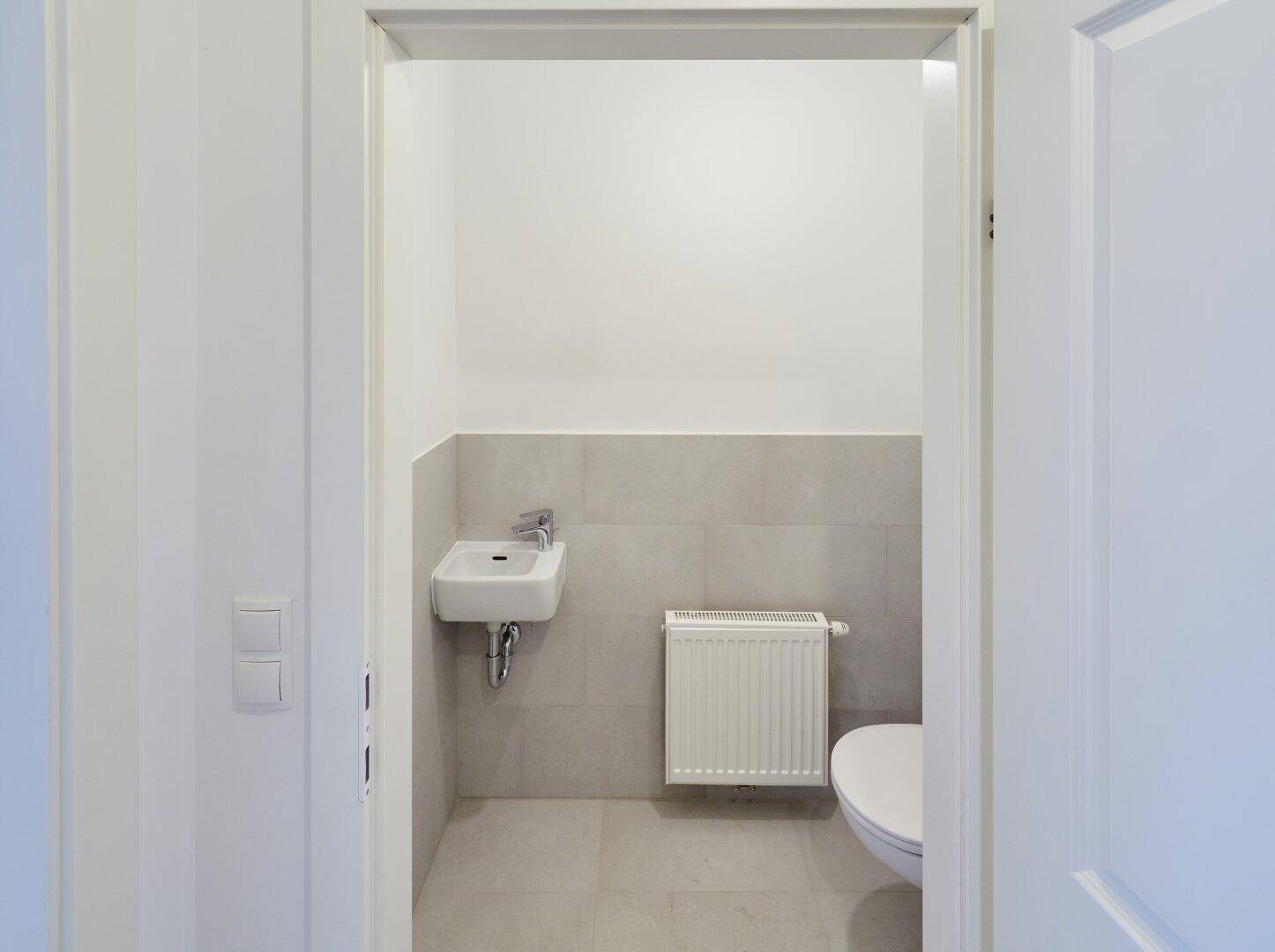 Kleines Gäste-WC mit Wand-WC, Waschbecken und Heizkörper, in modernem Design.