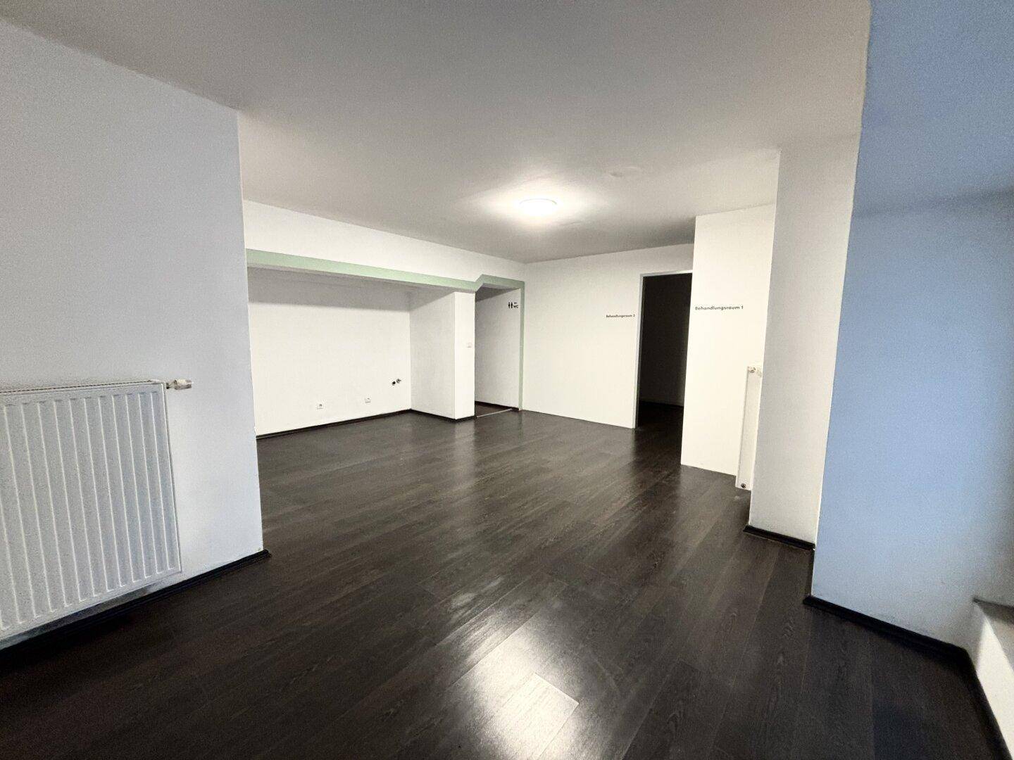 Geräumiger Wohnbereich mit dunklem Holzboden und weiß gestrichenen Wänden, bereit zur Einrichtung.