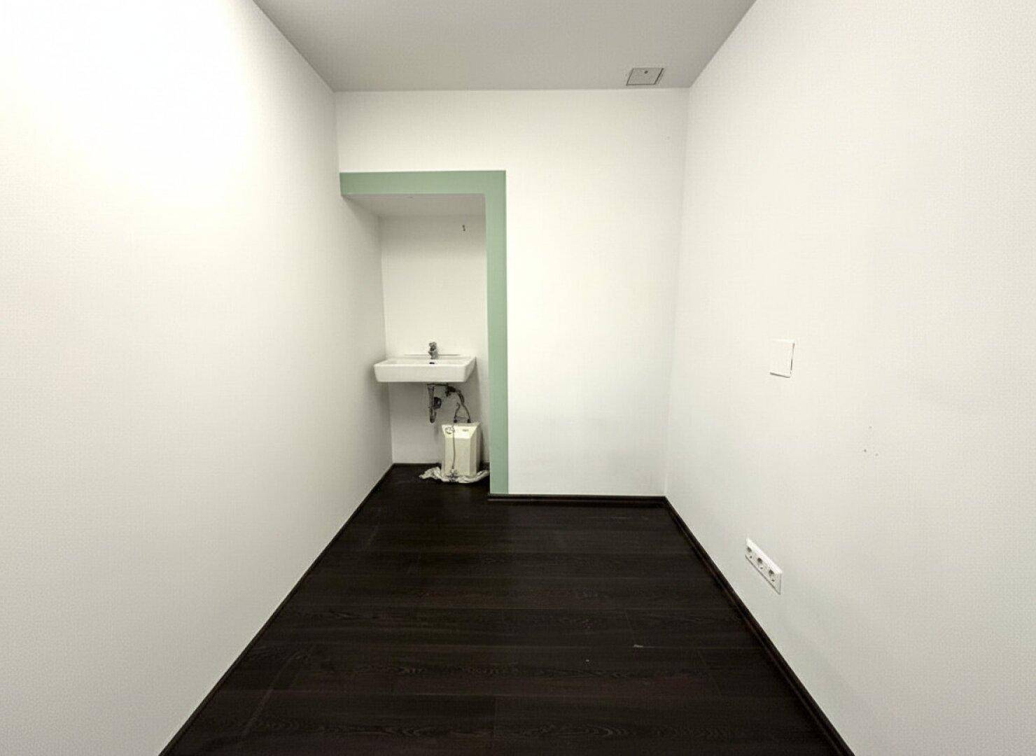 Kleiner Raum mit dunklem Holzboden und einem Waschbecken in einer Nische mit grüner Akzentwand.