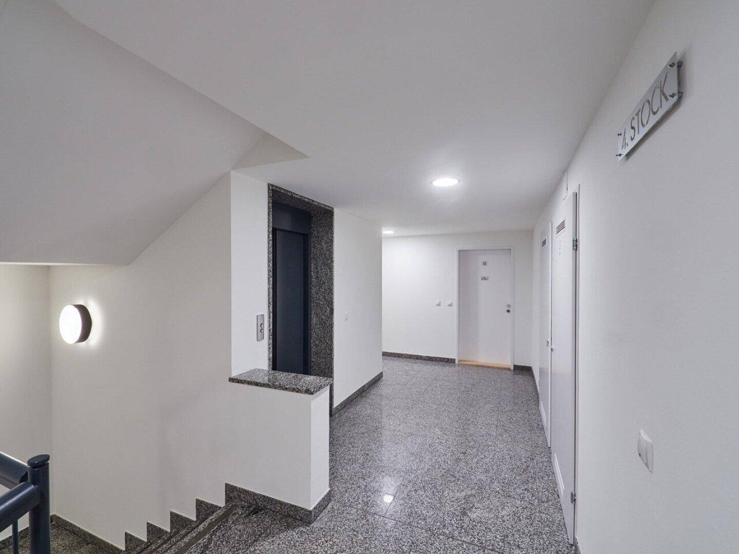 Geräumiger Hausflur mit Aufzug und Treppe, ausgestattet mit robustem Granitboden.