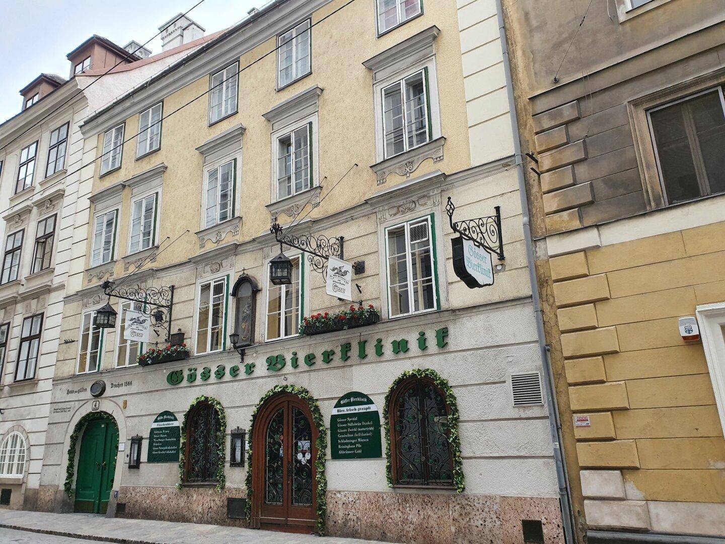 Altes Gebäude mit gelber Fassade und großen Fenstern an einer Kopfsteinpflastergasse.