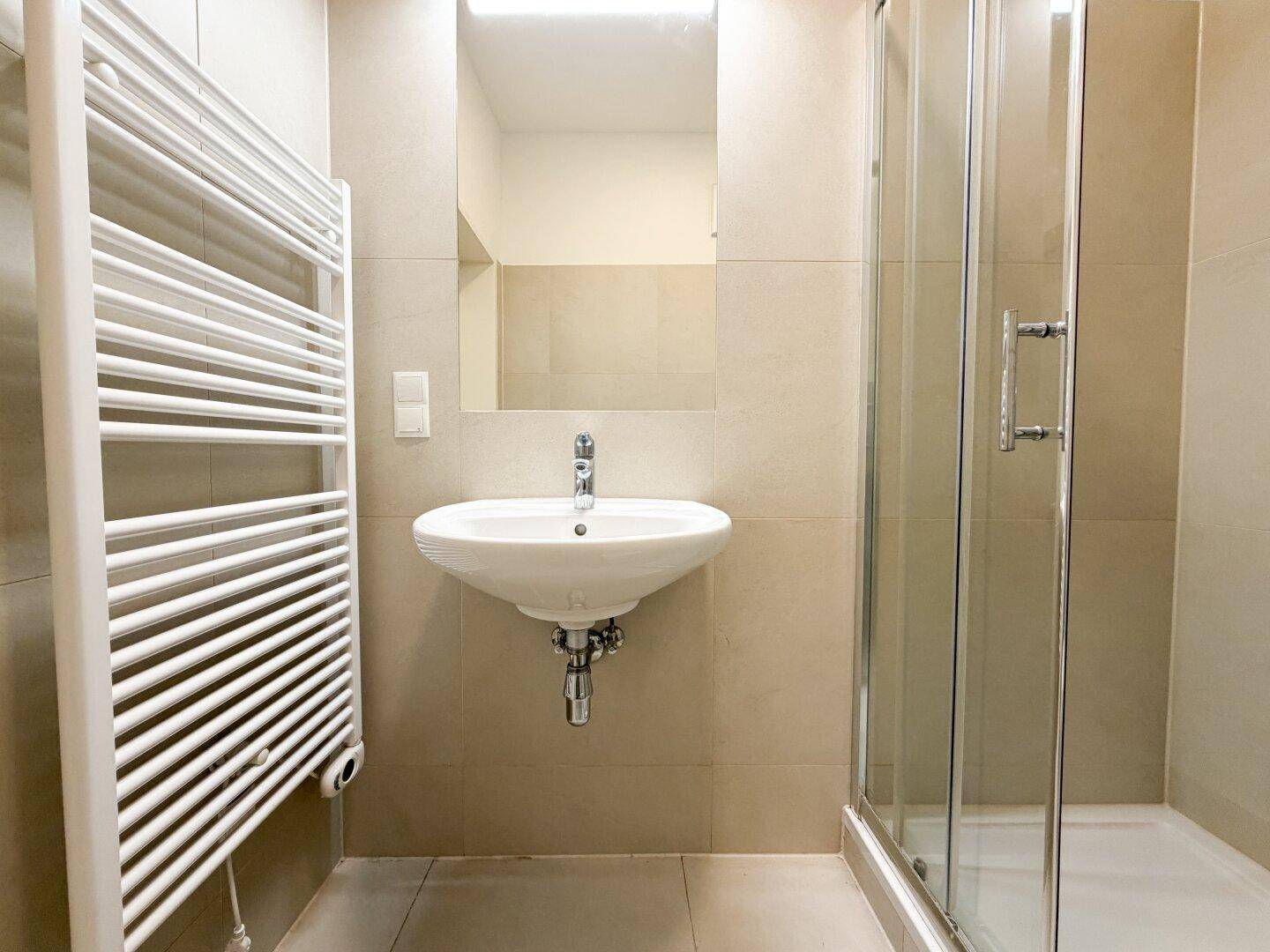 Modernes Badezimmer mit Duschkabine, Waschbecken, Spiegel und beheiztem Handtuchhalter.