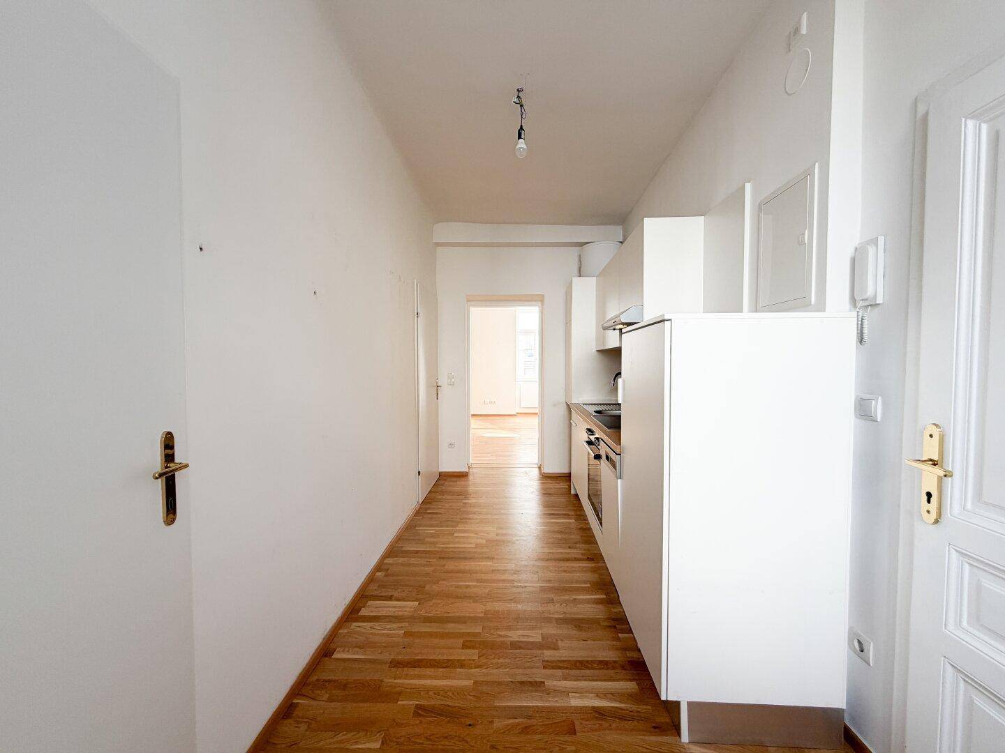 Langer Flur mit integrierter Küchenzeile, Holzboden und Zugang zu weiteren Räumen.