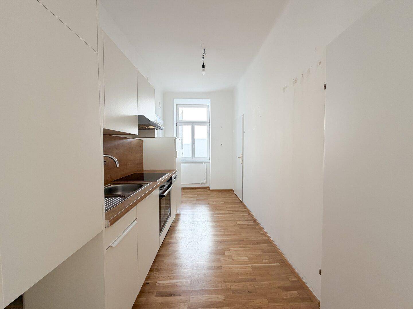 Heller Flur mit Küchenzeile und Fenster am Ende, das Tageslicht hereinlässt.
