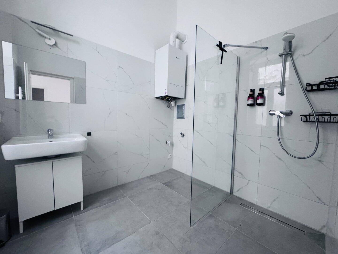 Modernes Badezimmer mit großformatigen Fliesen, ebenerdiger Dusche und wandhängendem Waschbecken.