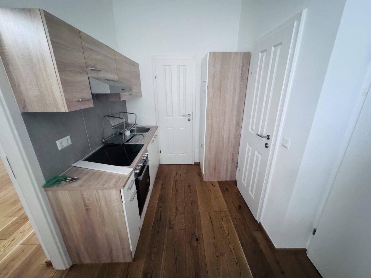 Kompakte Einbauküche mit Holzoptik-Schränken, Kochfeld und Backofen, ideal für kleine Wohnungen.