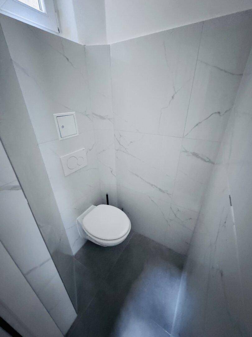 Modern gefliestes Gäste-WC mit Wand-WC und dunklem Boden, sauber und minimalistisch gestaltet.