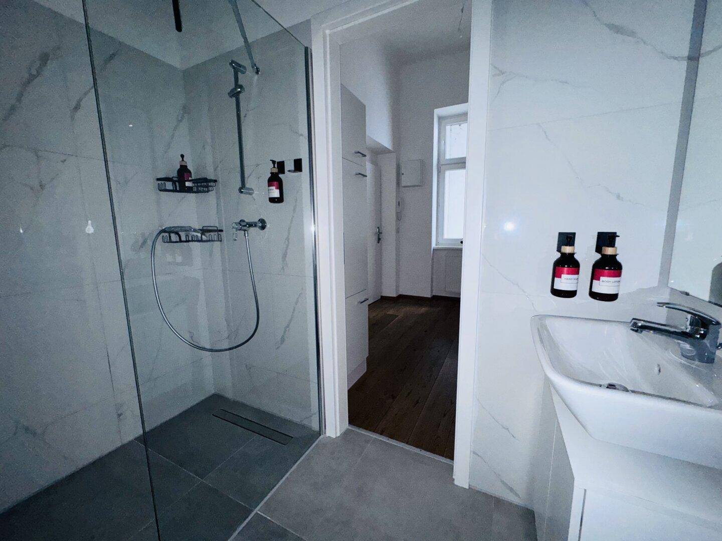 Modernes Badezimmer mit begehbarer Dusche, Glaswand und Waschbecken, hell und funktional.