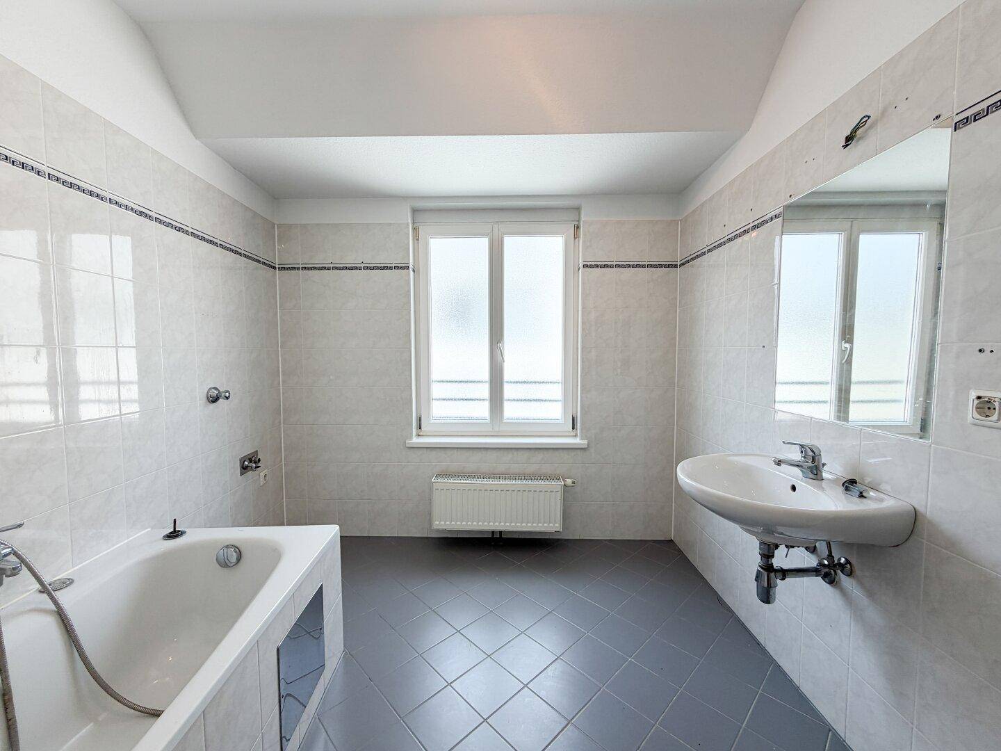 Geräumiges Badezimmer mit Badewanne, Waschbecken, Spiegel und Fenster.