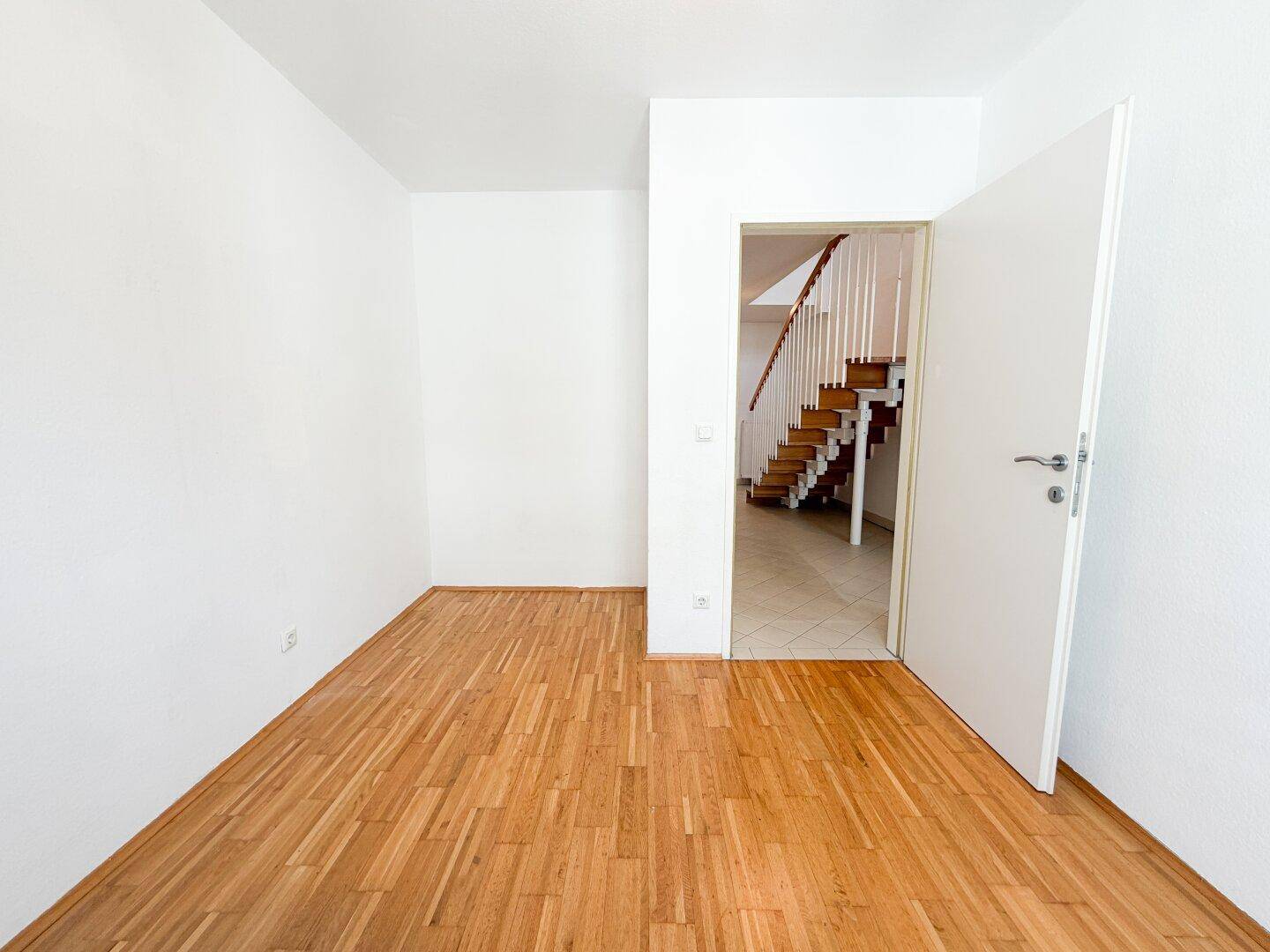 Leeres Zimmer mit Parkettboden und Zugang zu einem Treppenhaus.