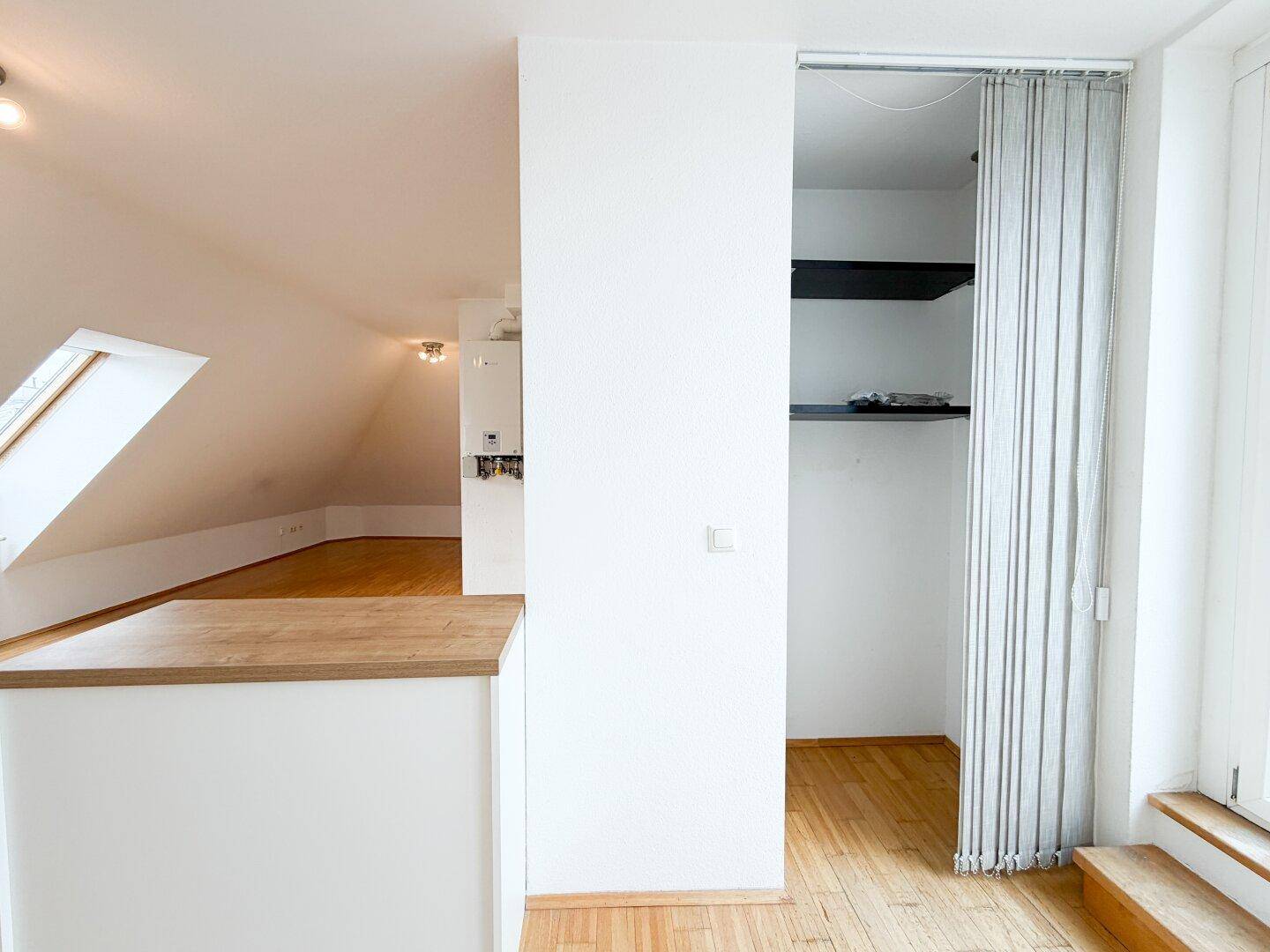 Offener Bereich mit Holzboden, Dachschräge und einem integrierten Schrank mit Vorhang.