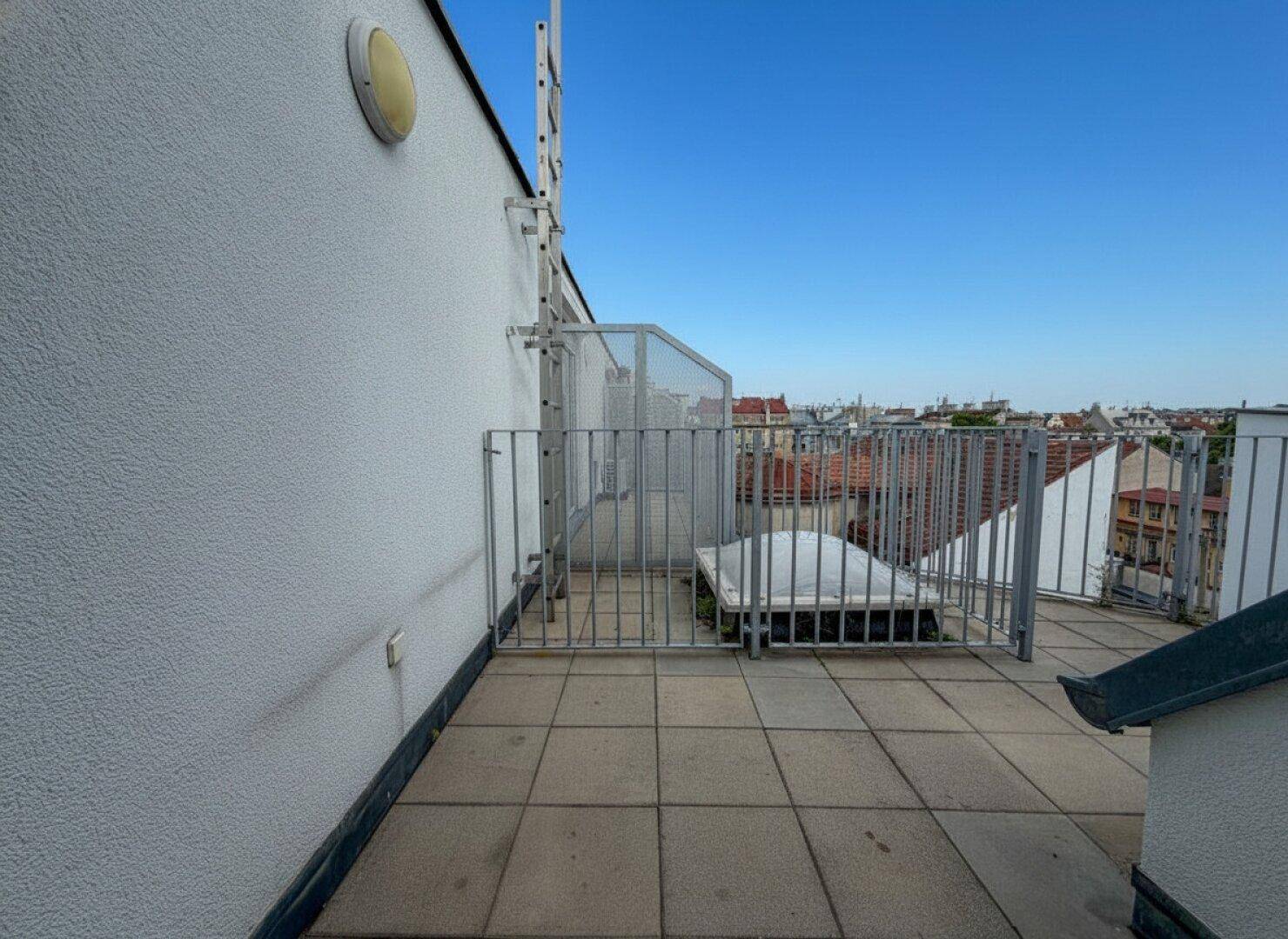 Dachterrasse mit Fliesenboden, Metallgeländer und weitem Blick über die Stadt.