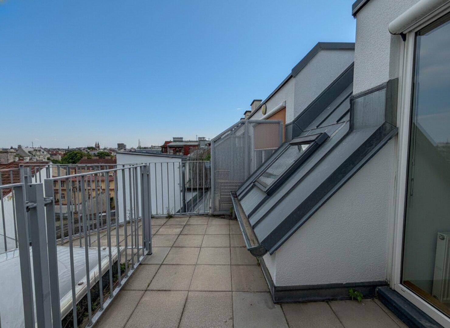 Geräumige Dachterrasse mit Fliesenboden, Dachfenstern und Panoramablick auf die Stadt.