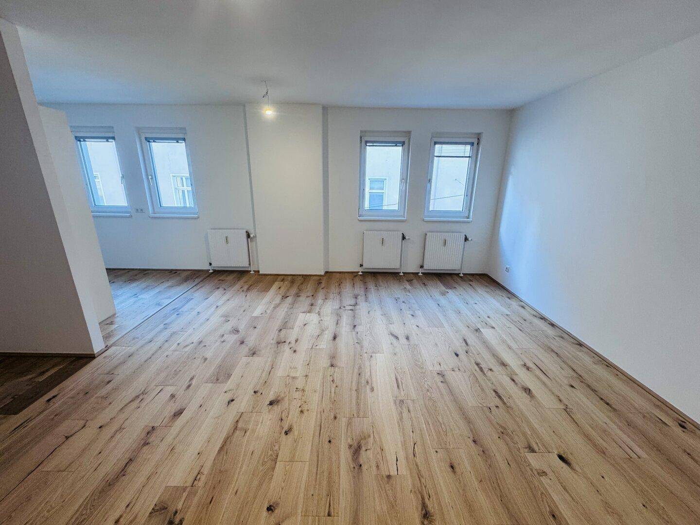 Geräumiger, heller Raum mit Holzboden und mehreren Fenstern, bereit zur individuellen Gestaltung.