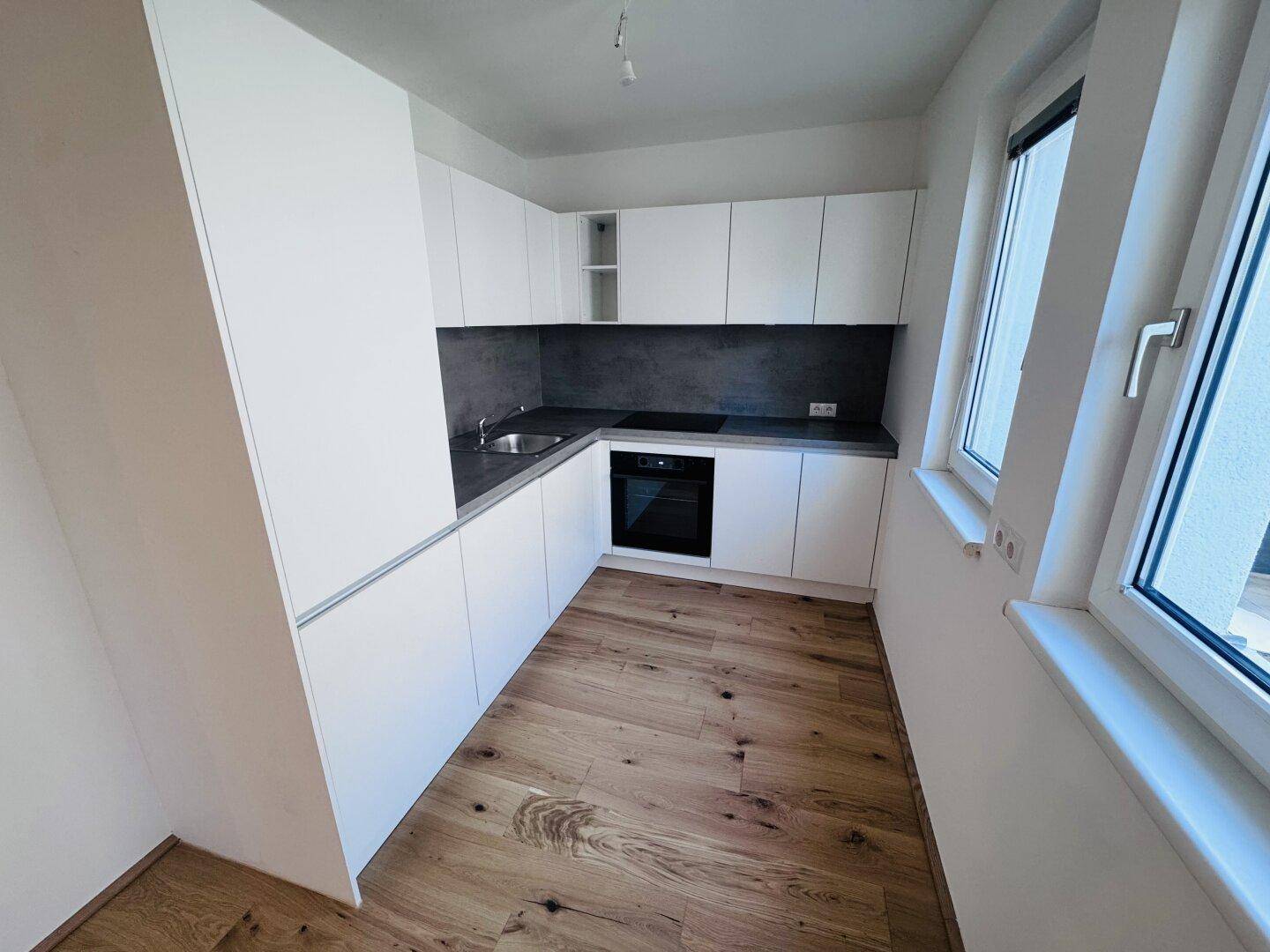 Moderne Einbauküche mit weißen Schränken, dunkler Arbeitsplatte und integriertem Backofen.