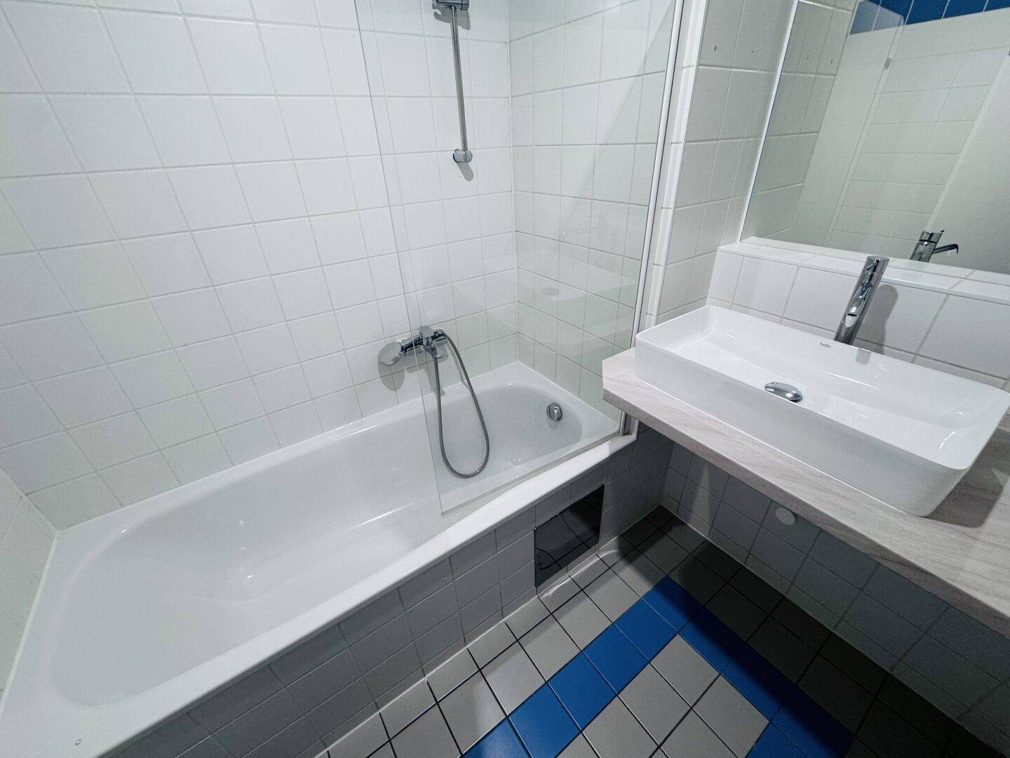 Modernes Badezimmer mit Badewanne, Duschvorrichtung und weiß-blauen Fliesen.