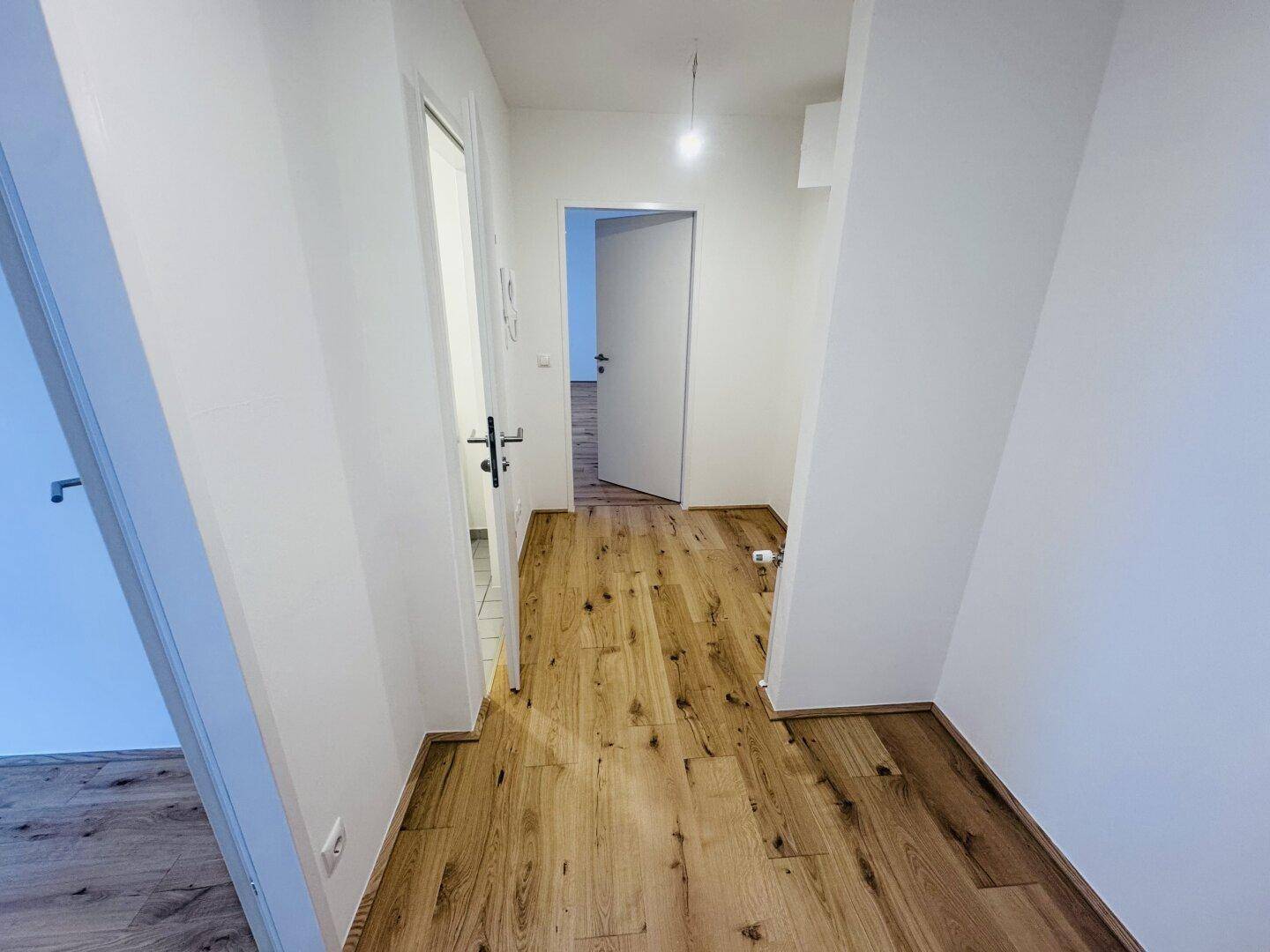 Heller Flur mit Holzboden und Zugang zu verschiedenen Räumen der Wohnung.