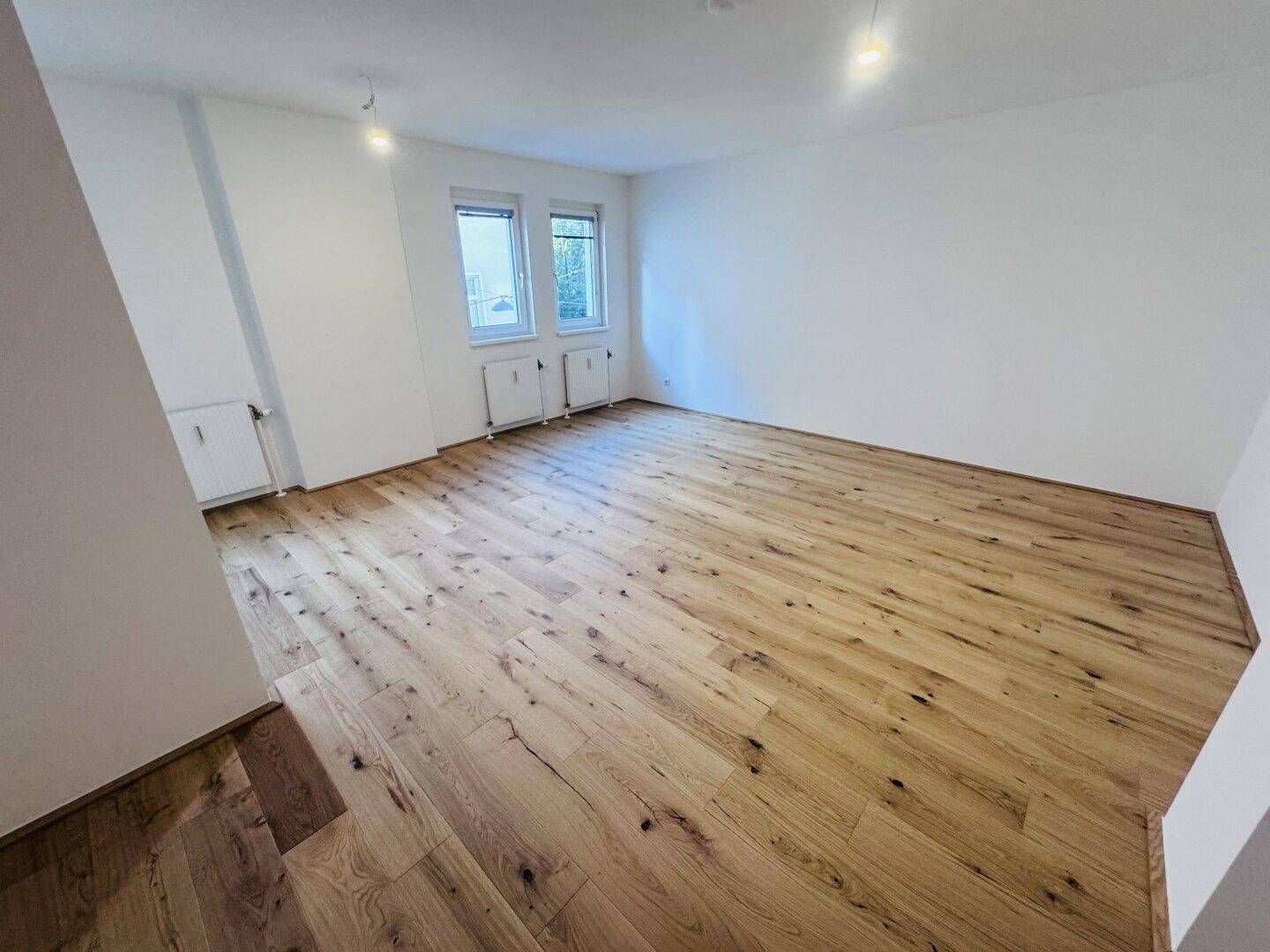 Großer, lichtdurchfluteter Raum mit Holzboden und Fenstern, ideal für Wohn- oder Schlafzimmer.