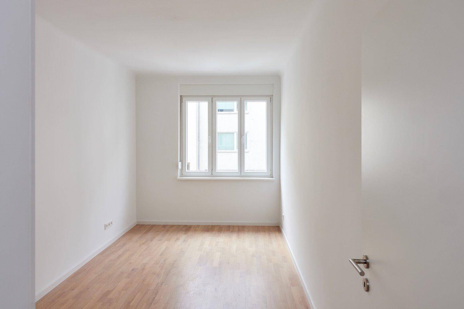 Helles, leeres Zimmer mit weißen Wänden und hellem Holzfußboden, bereit zur individuellen Gestaltung.