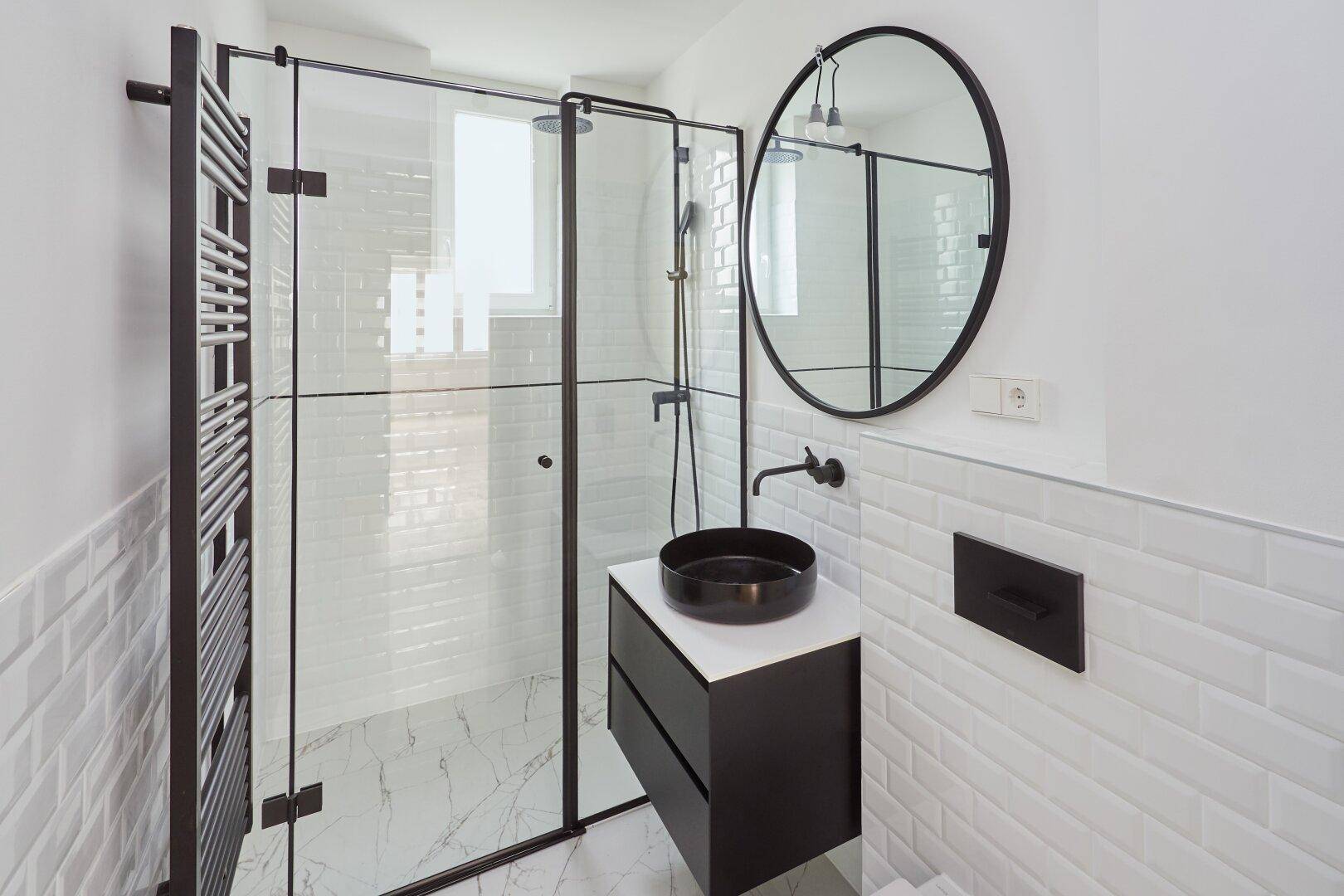 Modernes Badezimmer mit begehbarer Dusche, schwarzen Armaturen und stilvollem runden Spiegel.