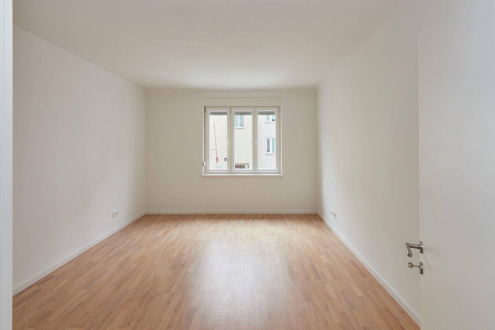 Geräumiges, helles Zimmer mit Parkettboden und großen Fenstern, ideal für Wohn- oder Schlafbereich.