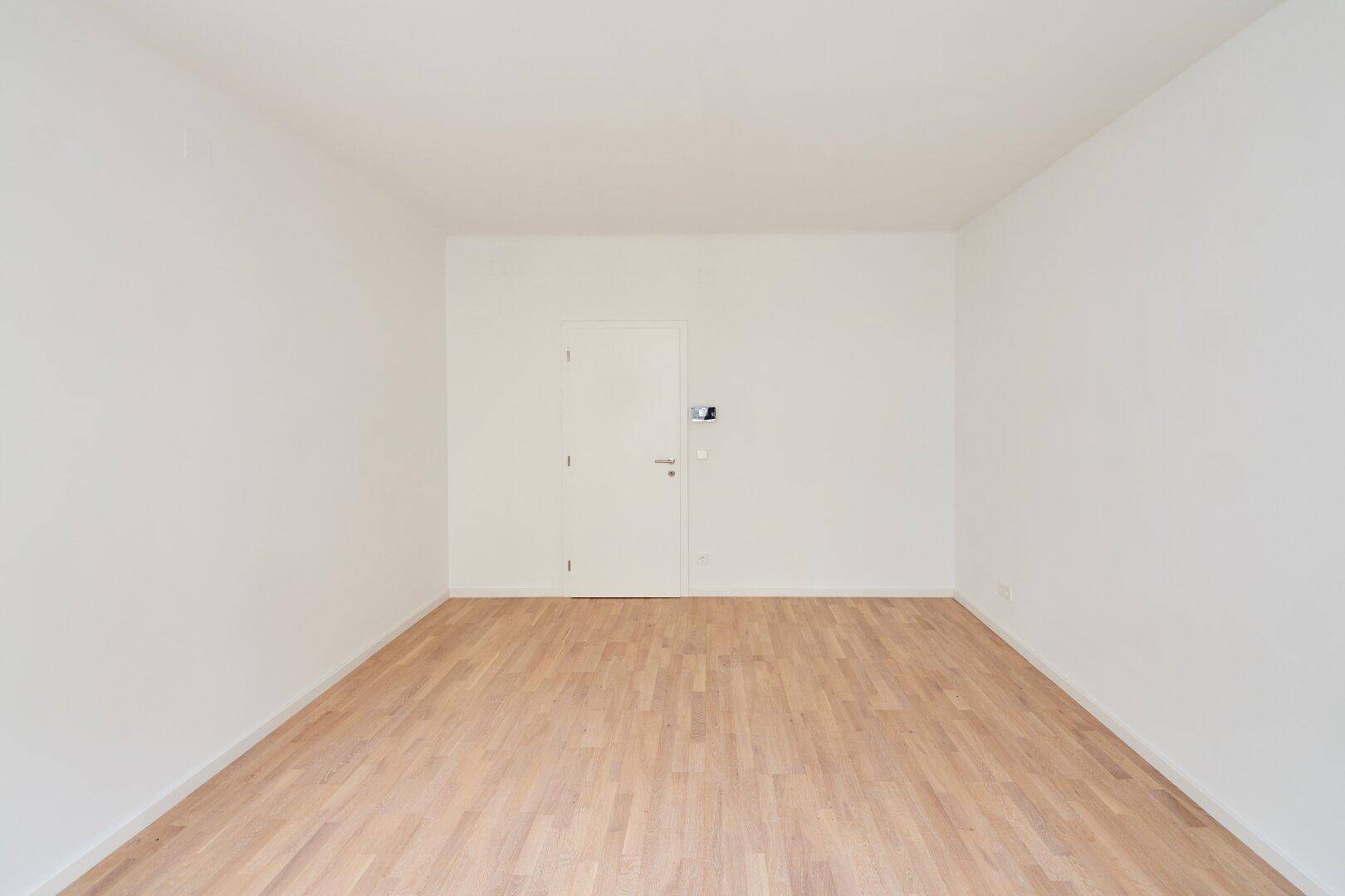 Leeres Zimmer mit hellem Parkettboden und weißen Wänden, bereit zur individuellen Einrichtung.