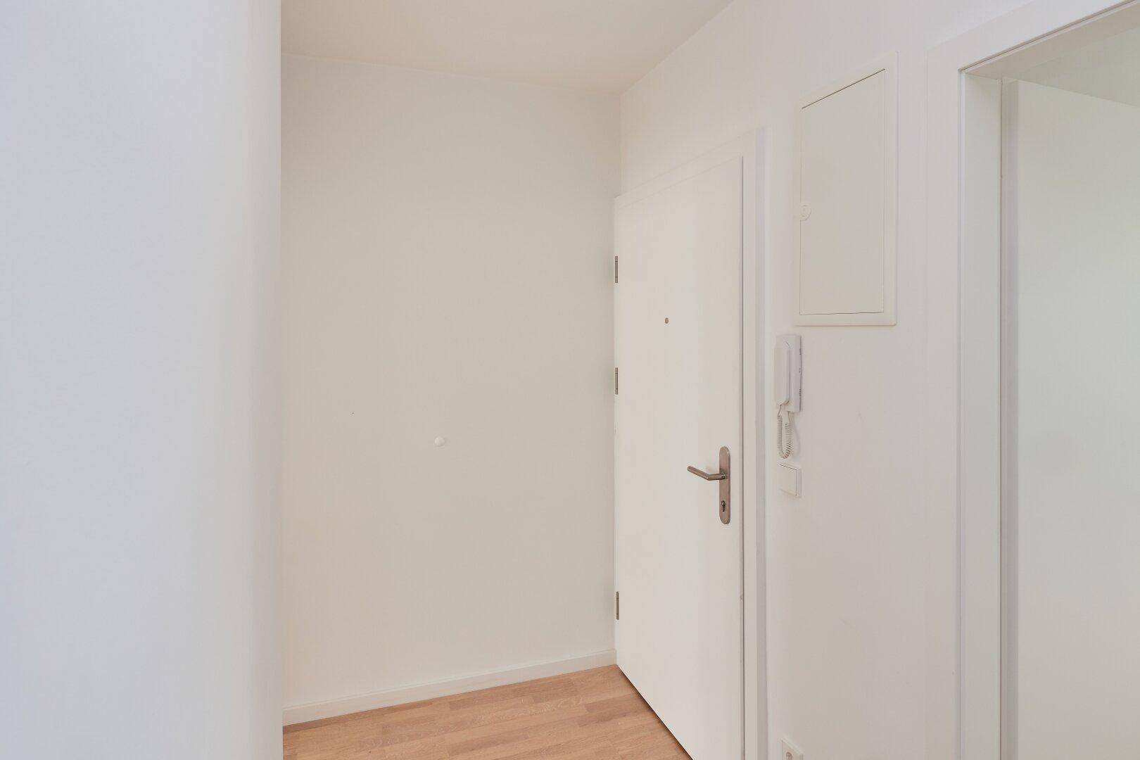 Heller Eingangsbereich mit Parkettboden und weißer Eingangstür, einladend gestaltet.