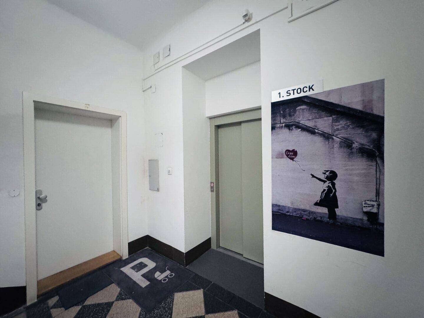 Eingangsbereich mit Aufzug und Banksy-Kunstdruck, der zu den oberen Etagen führt.