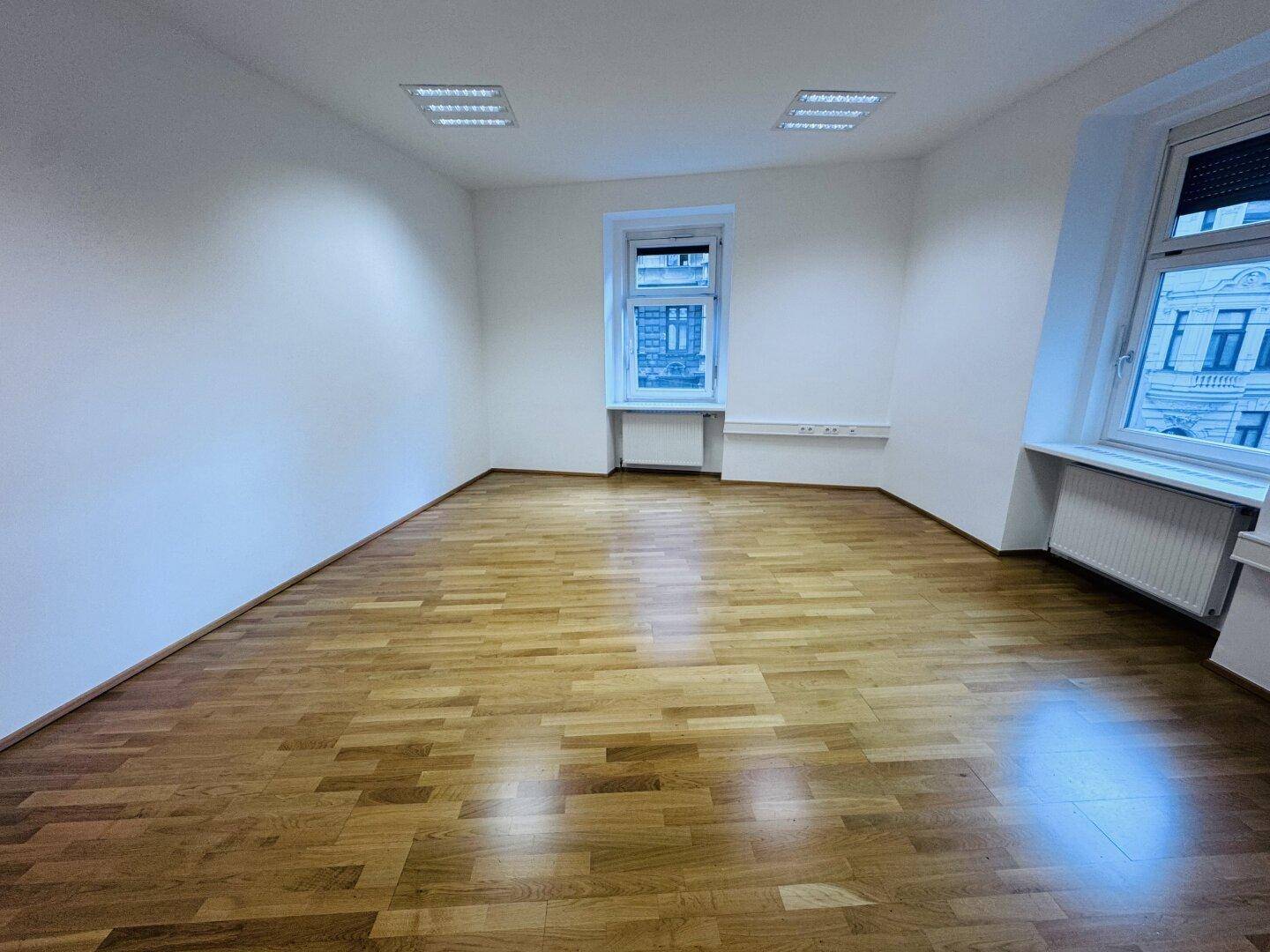 Geräumiger Büroraum mit einem großen Fenster und Holzparkett, bietet viel Platz und Helligkeit.