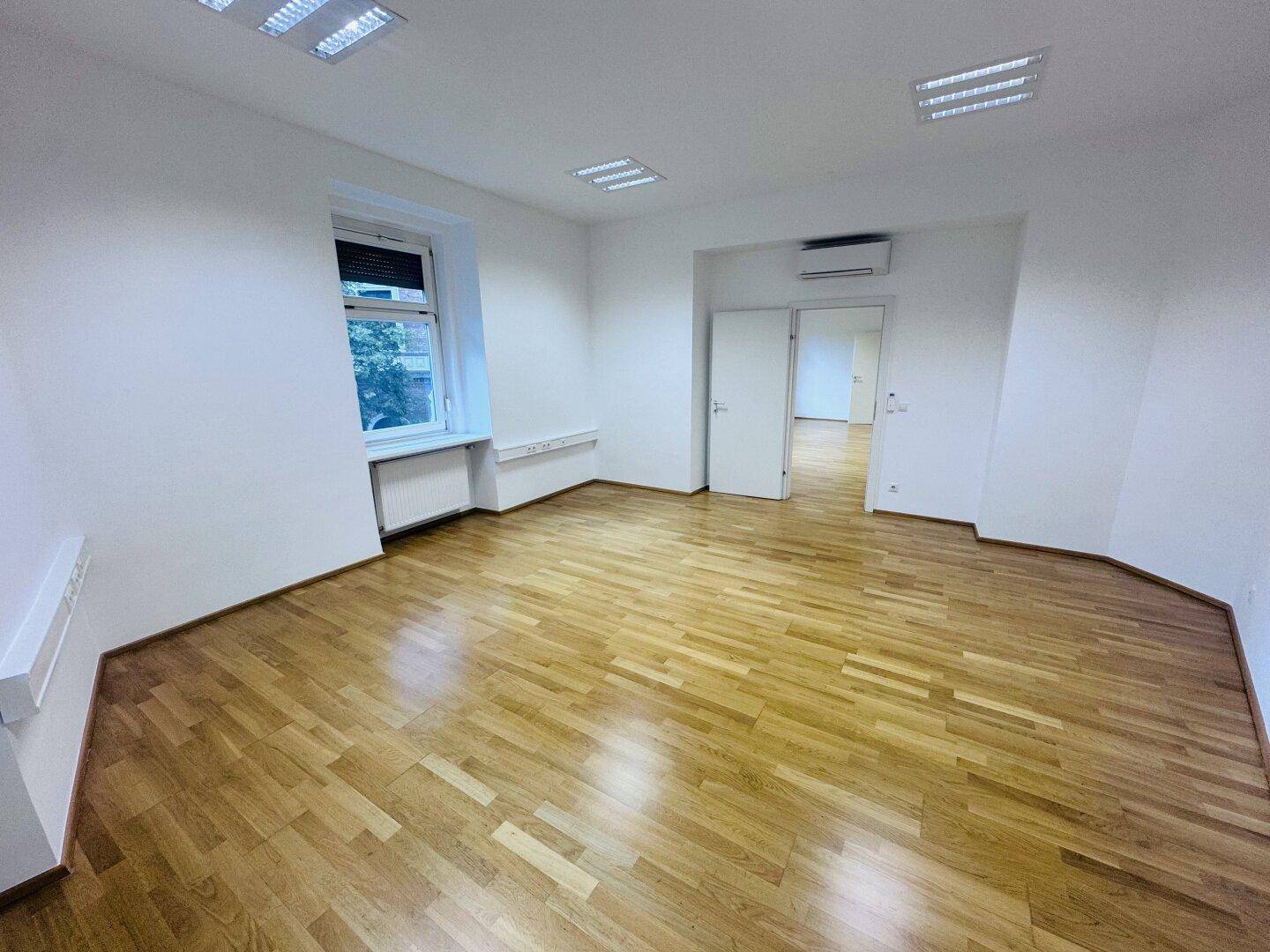 Heller Büroraum mit Holzparkett und Klimaanlage, bietet Komfort und eine angenehme Arbeitsumgebung.