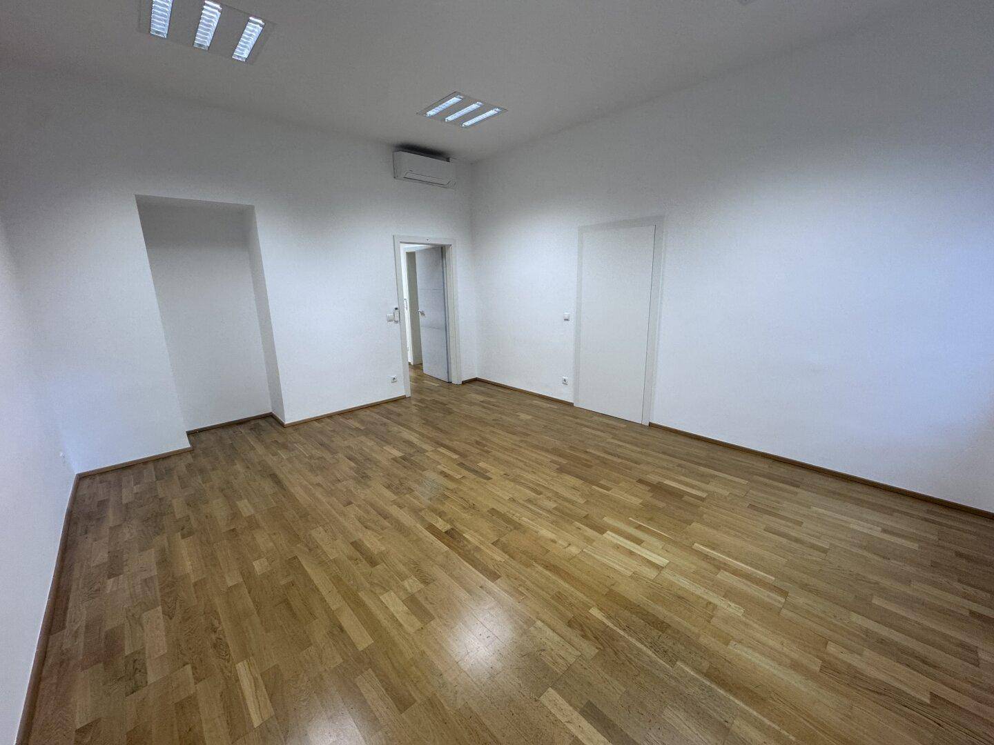 Heller Büroraum mit Holzparkett und Klimaanlage, bietet Komfort und eine angenehme Arbeitsumgebung.