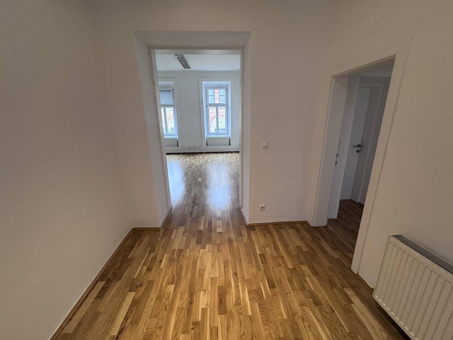 Heller Flur mit Holzboden, der den Blick in einen weiteren Raum mit Fenstern freigibt.
