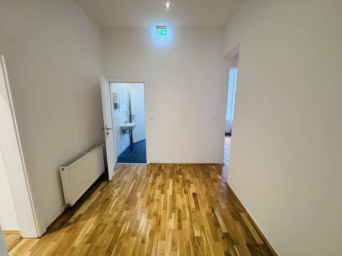 Flur mit Holzboden und einem Ausgangsschild, der zu einem Badezimmer führt.